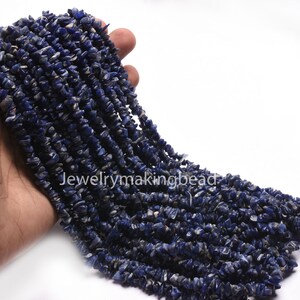Puede incluir: Un puñado de cuentas de piedras preciosas de color azul oscuro, de forma irregular. Las cuentas son pequeñas, con una superficie rugosa y texturizada. La imagen muestra múltiples hebras de las cuentas, lo que sugiere que son para la fabricación de joyas. El texto "Jewelrymakingbead" es visible.