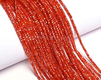 May include: Strands of faceted, orange-red gemstone beads. The beads are small and uniform in size, strung together to create a flowing, textured appearance. The beads are likely used for jewelry making.