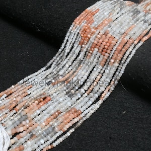 May include: Multiple strands of small, faceted beads in white, peach, and grey. The beads are strung together, creating a flowing, textured appearance. These beads are likely for jewellery making.