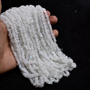 Può includere: Una collana di perle di pietra di luna bianca, ogni perla è di forma piccola e irregolare. Le perle sono infilate per formare una lunga collana.