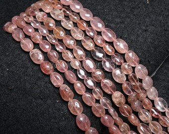 May include: Strands of oval-shaped, translucent pink gemstones. The beads have a polished finish and vary in shades of pink and peach. The gemstones are strung together, creating a beautiful display of natural color and texture. The image is taken on a black surface.