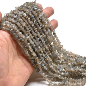 Puede incluir: Una hebra de chips de piedra preciosa de labradorita gris e iridiscente. Las virutas son de forma irregular y tienen una textura natural y rugosa.
