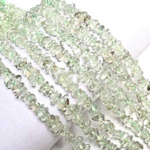 May include: Strands of light green gemstone beads. The beads are irregularly shaped and have a translucent quality, with variations in color and texture. The beads are strung together, creating a flowing, organic appearance. The overall effect is delicate and natural.