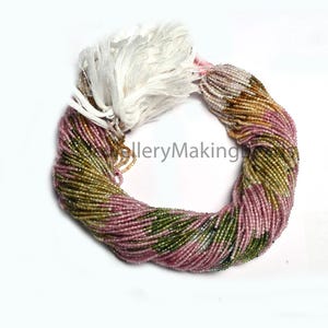 May include: A circular strand of small, faceted tourmaline beads featuring a gradient of colours including pink, green, and golden-brown. The beads are strung together on a thin cord and secured with a white tassel at the top of the loop.