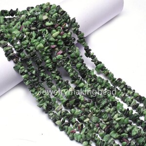 Op de afbeelding: Strengen groene en zwarte edelsteen kralen met kleine roze vlekken. De kralen zijn onregelmatig van vorm en lijken aan elkaar geregen te zijn. De tekst "Jewelrymakingbead" is zichtbaar.