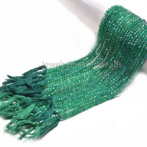 May include: A strand of faceted, emerald green beads with a tassel at the end. The beads are small and evenly cut, reflecting light. The tassel is a darker shade of green, adding contrast. The beads are likely used for jewelry making.