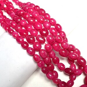 May include: Strands of oval-shaped, vibrant pink beads. The beads are strung together, creating a flowing, textured appearance. The image is well-lit, highlighting the glossy surface of the beads. The beads are likely for jewelry making.