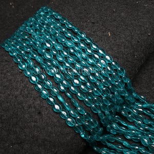 May include: Strands of translucent, teal-colored oval beads. The beads are strung together, creating a flowing, textured appearance. The beads are likely for jewelry making.