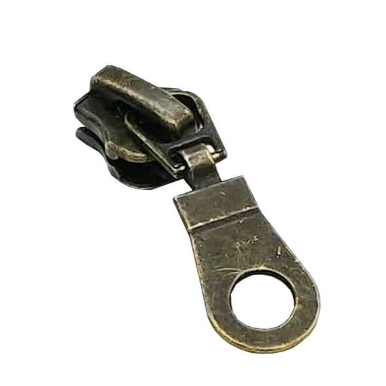 May include: Antique gold zipper pull with a ring. The pull is made of metal and has a worn, aged look.
