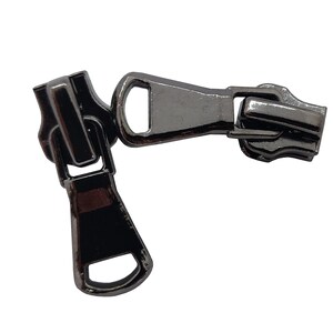 May include: A black metal zipper pull with a slider and a loop. The zipper pull is designed to be used with a zipper on a garment or other item.