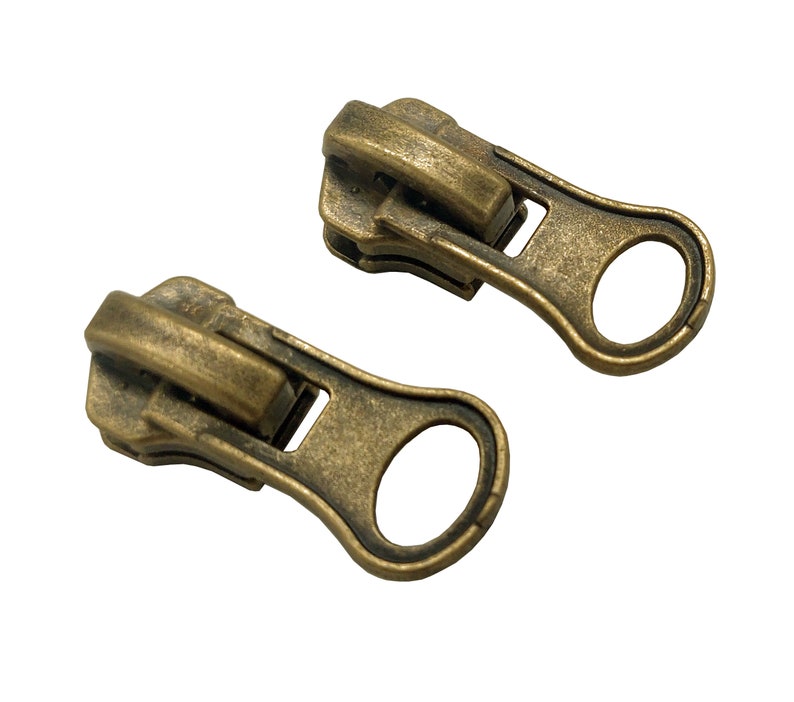 May include: Two antique gold zipper pulls with a loop on the end. The zipper pulls are made of metal and have a worn, aged look.