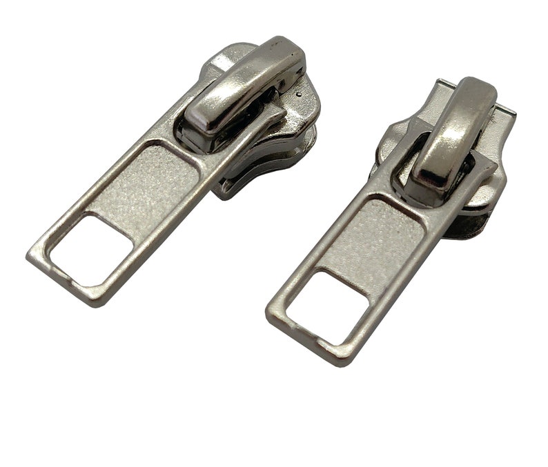 May include: Two silver zipper pulls with a rectangular shape and a square opening in the center. The pulls have a smooth, metallic finish.