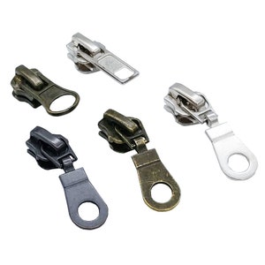 May include: Five zipper pulls in different colors: silver, black, bronze, and two shades of brown. The pulls have a loop at the bottom and a slider at the top.