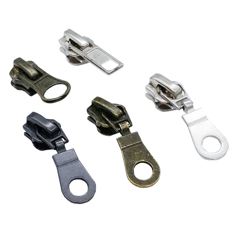 May include: Five zipper pulls in different colors: silver, black, bronze, and two shades of brown. The pulls have a loop at the bottom and a slider at the top.