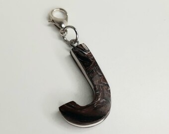 May include: A wooden letter J charm with a silver finish and a silver lobster clasp. The letter J is dark brown with a white swirl pattern.