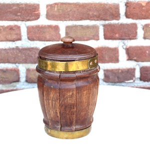 May include: A small, wooden barrel-shaped container with a lid and brass bands. The container is made of dark brown wood and has a rounded shape. The lid has a small wooden knob. The brass bands add a decorative touch to the container.