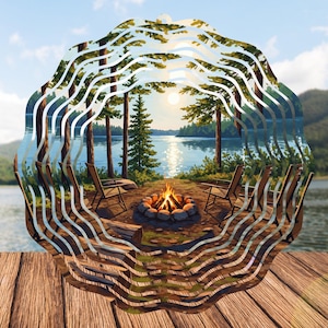 May include: A decorative metal wind spinner featuring a lakeside campfire scene. The image shows a fire pit with chairs, trees, and a lake. The design is layered with a wavy, circular frame, creating a 3D effect. The background shows a lake and trees.