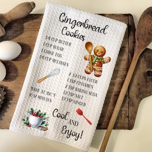May include: White kitchen towel with a gingerbread man illustration and a recipe for gingerbread cookies. The recipe includes ingredients like butter, sugar, molasses, flour, cinnamon, baking soda, salt, and ginger. The towel also says "Bake at 350 degrees F for 10-12 minutes" and "Cool and Enjoy!"