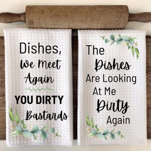 May include: Two white waffle-weave kitchen towels with black text that reads "Dishes, We Meet Again YOU DIRTY Bastards" and "The Dishes Are Looking At Me Dirty Again." Each towel has a floral design.