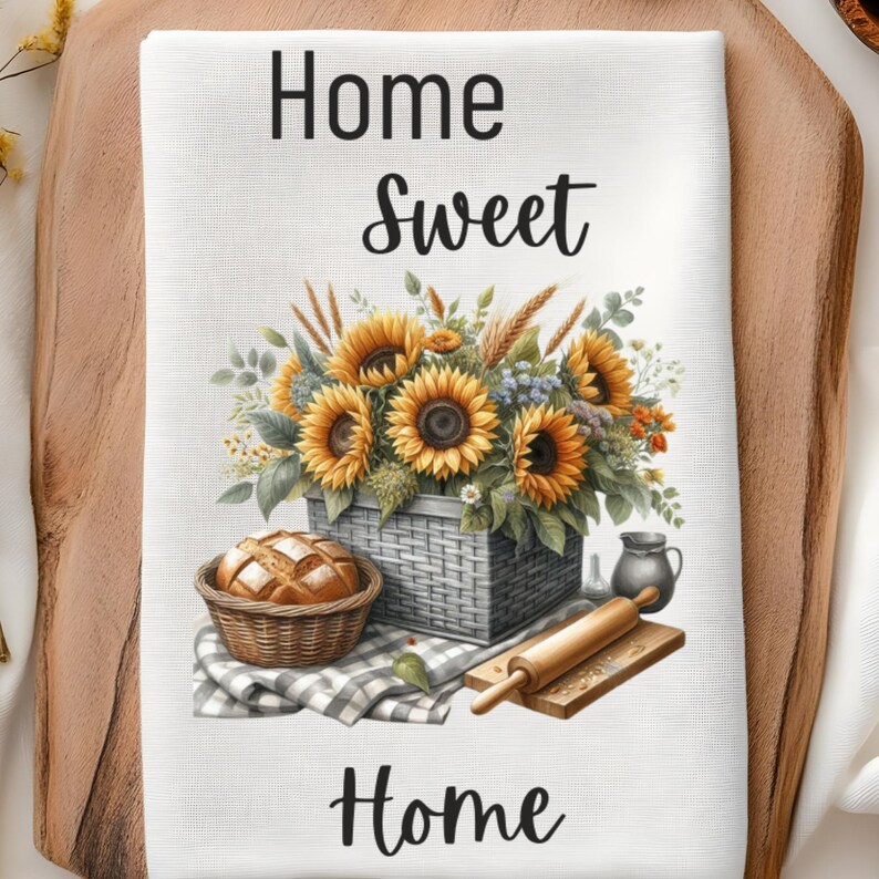 Puede incluir: Una toalla de cocina blanca con el texto "Home Sweet Home" impreso en negro. La toalla presenta una ilustraci&oacute;n de acuarela de una cesta de girasoles, una hogaza de pan en una cesta y un rodillo.