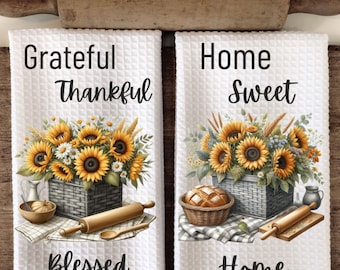 May include: Two white kitchen towels with sunflower and wheat designs. The first towel says "Grateful Thankful Blessed" and the second towel says "Home Sweet Home".