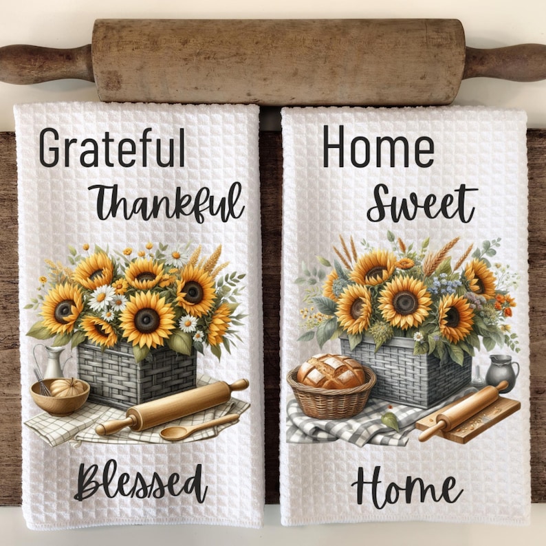 Puede incluir: Dos toallas de cocina blancas con dise&ntilde;os de girasoles y trigo. La primera toalla dice "Grateful Thankful Blessed" y la segunda toalla dice "Home Sweet Home".