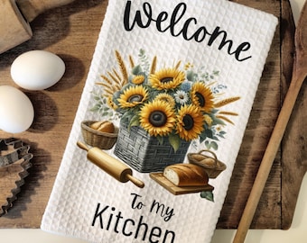 May include: White kitchen towel with a sunflower and wheat design. The towel has the text "Welcome to my Kitchen" printed on it.