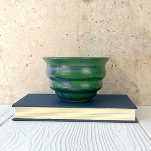 May include: A green and purple ceramic planter with a wavy design. The planter is sitting on top of a blue book.