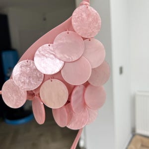 Puede incluir: Top de bikini rosa claro con dise&ntilde;o de cuello halter. El top est&aacute; adornado con m&uacute;ltiples discos redondos, iridiscentes y rosas. Los discos est&aacute;n sujetos al top con peque&ntilde;os lazos. El top de bikini est&aacute; hecho de un material suave y liso.