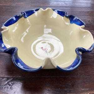 May include: A ceramic bowl with a cream-coloured interior and a deep blue scalloped rim. The centre of the bowl features a small, hand-painted design of a cluster of red berries on a thin green stem, adding a subtle detail to the smooth surface.