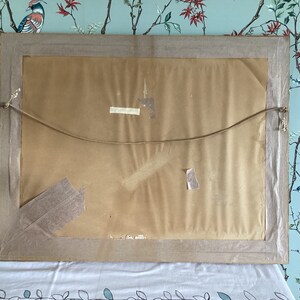 Peut inclure: L'arri&egrave;re d'un tableau encadr&eacute; avec un fond en papier brun. Le cadre est en bois et a une finition brun clair. Il y a deux morceaux de ruban adh&eacute;sif au dos du tableau.