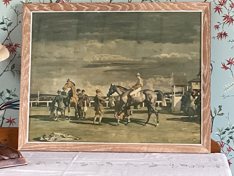 Peut inclure: Une estampe vintage encadr&eacute;e repr&eacute;sentant une sc&egrave;ne de course de chevaux. L'estampe montre un jockey mont&eacute; sur un cheval brun, avec d'autres chevaux et des personnes en arri&egrave;re-plan. La sc&egrave;ne se d&eacute;roule sous un ciel nuageux.