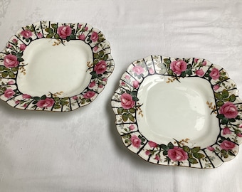 May include: Two white square ceramic plates with a black and gold trim. The plates have a floral design with pink roses and green leaves.