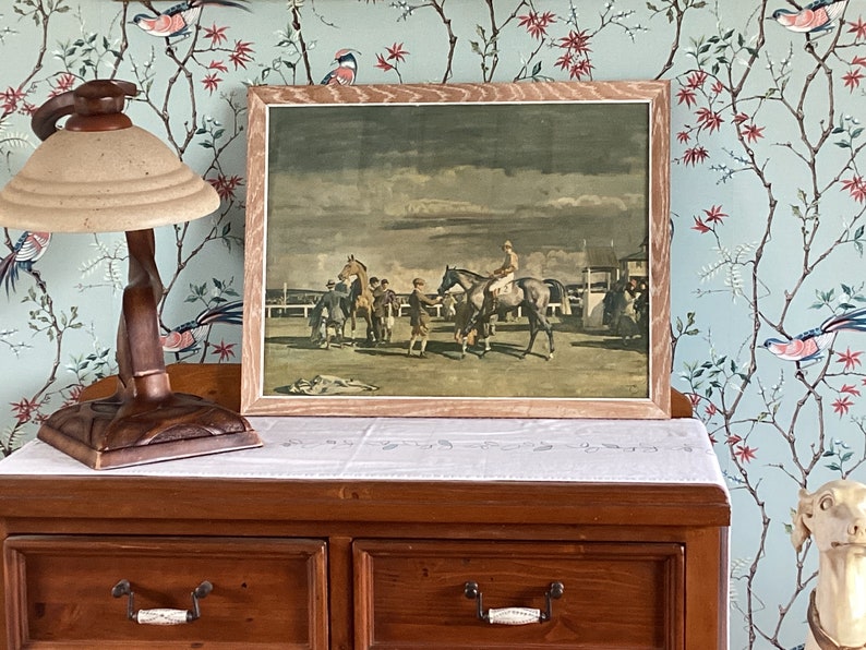 Peut inclure: Une estampe vintage encadr&eacute;e repr&eacute;sentant une sc&egrave;ne de course de chevaux. L'estampe repr&eacute;sente un groupe de chevaux et de cavaliers en course, avec une foule de personnes regardant en arri&egrave;re-plan. L'estampe est dans un cadre en bois avec une finition brun clair.