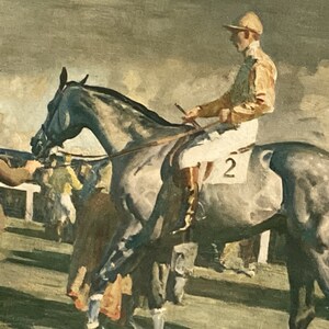 Peut inclure: Un jockey v&ecirc;tu d'une tenue de course marron et jaune monte un cheval gris avec le num&eacute;ro "2" blanc sur le c&ocirc;t&eacute;. Le cheval est dans une &eacute;curie avec d'autres personnes et chevaux en arri&egrave;re-plan.