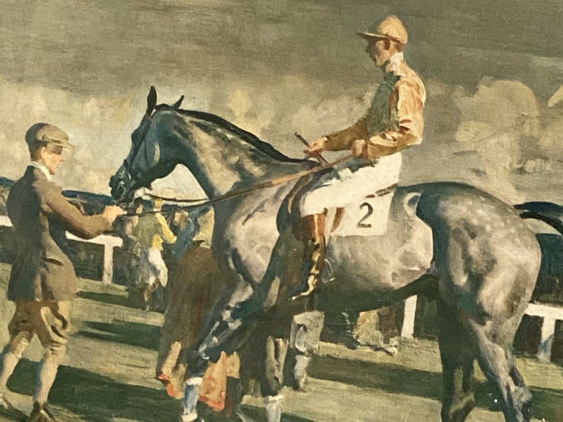 Peut inclure: Un jockey v&ecirc;tu d'une tenue de course marron et jaune monte un cheval gris avec le num&eacute;ro "2" blanc sur le c&ocirc;t&eacute;. Le cheval est dans une &eacute;curie avec d'autres personnes et chevaux en arri&egrave;re-plan.