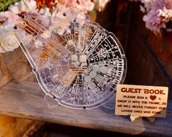 Könnte beinhalten: Ein transparentes Acryl-Gästebuch in Form des Millennium Falcon aus Star Wars. Das Gästebuch hat ein Schild mit der Aufschrift "GÄSTEBUCH BITTE SIGNIEREN SIE EIN HERZ & WERFEN SIE ES IN DEN RAHMEN. DAMIT WIR UNSERE LIEBEN, DIE GEKOMMEN SIND, NIEMALS VERGESSEN".