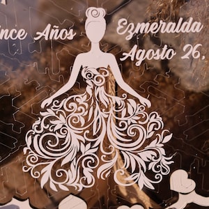 Pu&ograve; includere: Puzzle in acrilico trasparente con la silhouette di una donna in un abito con intricati motivi floreali. Il testo "Once A&ntilde;os" e "Ezmeralda Agosto 26" &egrave; inciso nell'acrilico. Il design include forme di cuore.