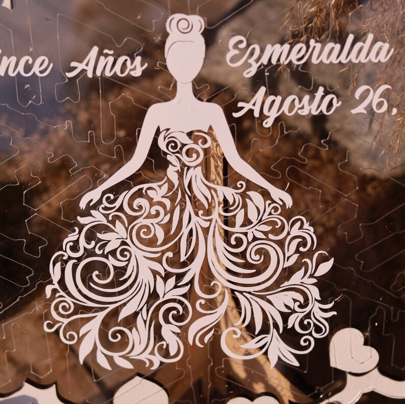 Pu&ograve; includere: Puzzle in acrilico trasparente con la silhouette di una donna in un abito con intricati motivi floreali. Il testo "Once A&ntilde;os" e "Ezmeralda Agosto 26" &egrave; inciso nell'acrilico. Il design include forme di cuore.