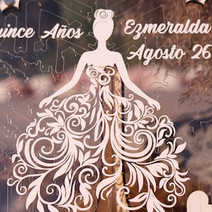 Pu&ograve; includere: Un pezzo decorativo in acrilico trasparente a forma di fiocco di neve. Presenta una silhouette ritagliata di una donna in abito con intricati disegni floreali. &Egrave; visibile anche il testo "Quince A&ntilde;os" e "Ezmeralda Agosto 26".