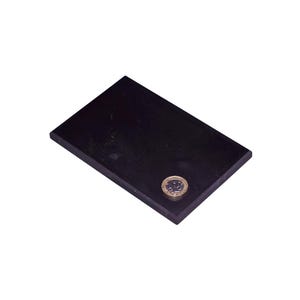 May include: A rectangular black slab with a smooth, dark surface. A single circular metallic coin is placed near the bottom right corner of the slab, providing a visual reference for the scale of the object against the dark, flat material.