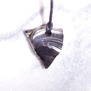 May include: A black obsidian pendant with a smooth, polished surface hangs from a black cord. The pendant is shaped like a teardrop and has a hole drilled through the top for the cord.