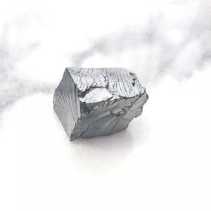 May include: A large, dark gray, irregularly shaped piece of raw, unpolished metal. The metal has a rough, textured surface.