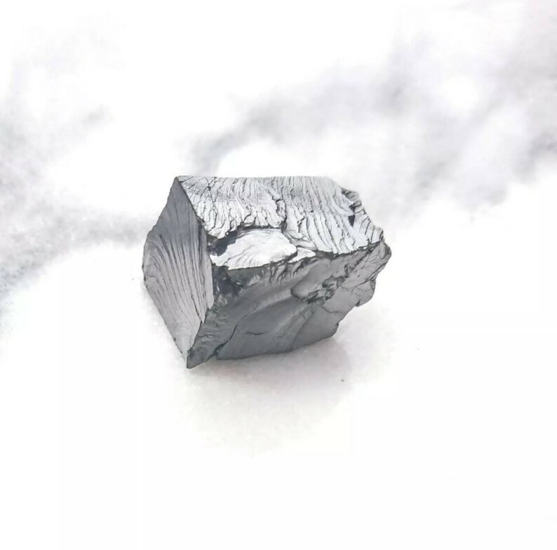 May include: A large, dark gray, irregularly shaped piece of raw, unpolished metal. The metal has a rough, textured surface.