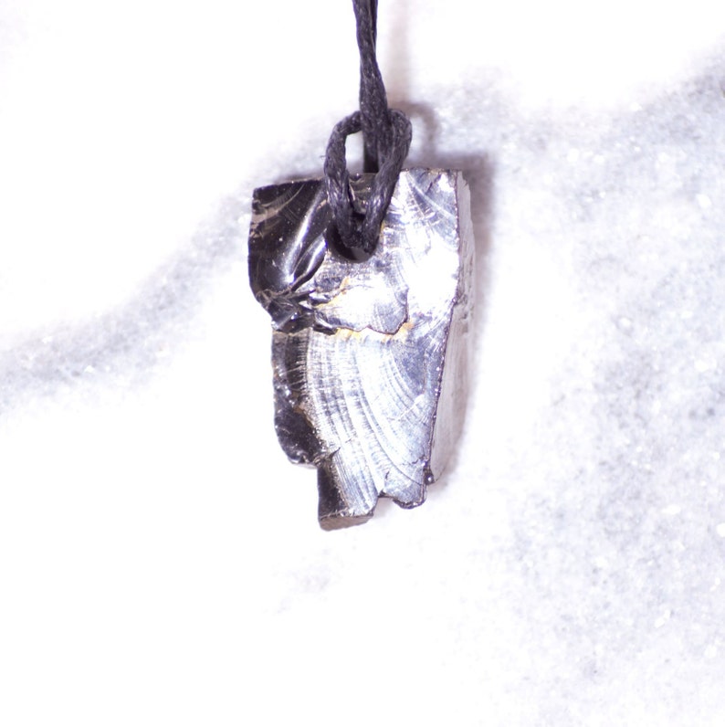 May include: A black obsidian pendant with a silver sheen hangs from a black cord. The pendant is irregularly shaped and has a rough texture.