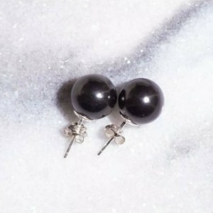 以下が含まれることがあります： 丸く磨かれた黒真珠のスタッドピアス一対。各真珠は銀色の金属ポストに取り付けられ、お揃いのバタフライ型キャッチが付いています。滑らかで光沢のある表面と、古典的な球体の形状が特徴です。