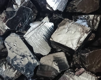 May include: A close-up of a pile of dark gray, metallic, irregularly shaped, and rough-textured stones.