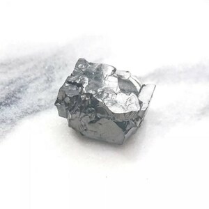 May include: A large, dark gray, irregularly shaped crystal with a metallic sheen. The crystal has many facets and appears to be a raw, unpolished stone.