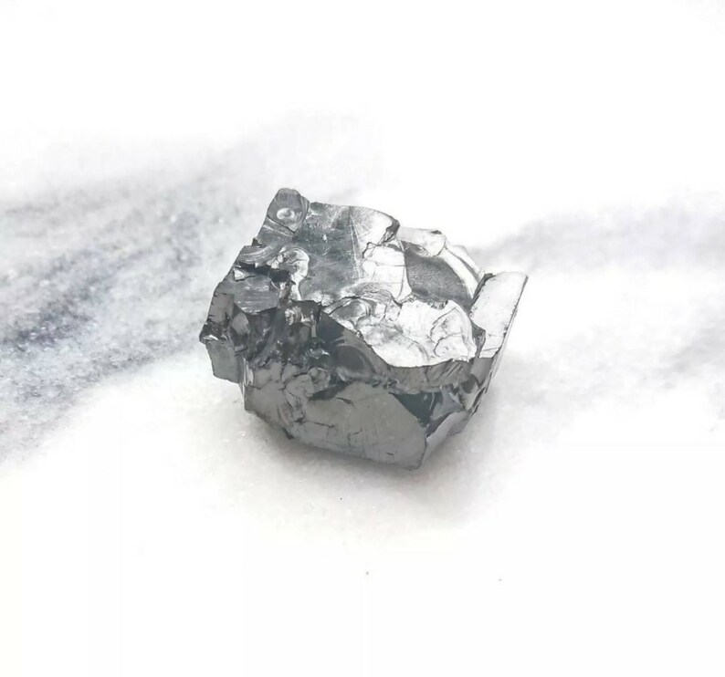May include: A large, dark gray, irregularly shaped crystal with a metallic sheen. The crystal has many facets and appears to be a raw, unpolished stone.