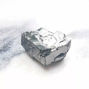 May include: A rough, gray, metallic rock with a crystalline structure. The rock has a jagged, irregular shape and appears to be a raw mineral specimen.